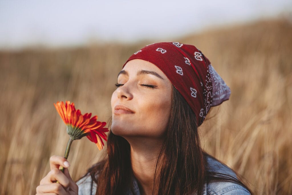 Beautiful young woman smells a flower in a meadow by John FRANCEY